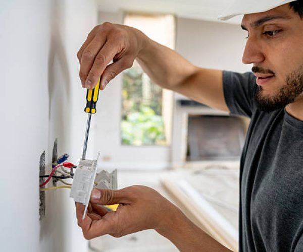 Latin American electrician installing a power socket while building a house and using a screwdriver